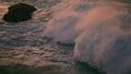 Splashing waves covering rock at sunset closeup. Cold sea water foaming evening