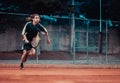 Split Croatia September 2020 Man playing tennis seen sprinting to catch the ball served short. Playing at night on an orange clay