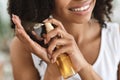 Split Ends Treatment. Smiling Black Woman Spraying Essential Oil On Curly Hair Royalty Free Stock Photo