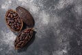 Split fermented cocoa pod with shelled cacao beans atop dark grey backdrop, top view