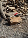 A splitting maul embedded in a log, surrounded by chopped and unchopped firewood on gravel under sunlight Royalty Free Stock Photo