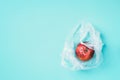 Spoiled bad red apple in plastic bag on blue background. Garbage dump rotten food. Top view. Copy space. Rotten vegetables and
