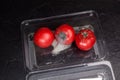 Spoiled tomatoes with mold in disposable plastic container. Organic food waste in supermarkets. Incorrect long-term storage. Dark