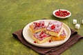 Sponge cake with red currant and blackberry jam, sprinkled with coconut, on a light earthen plate against an olive green concrete Royalty Free Stock Photo