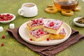 Sponge cake with red currant and blackberry jam, sprinkled with coconut, on a light earthen plate against an olive green concrete Royalty Free Stock Photo