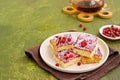 Sponge cake with red currant and blackberry jam, sprinkled with coconut, on a light earthen plate against an olive green concrete Royalty Free Stock Photo