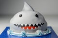 Sponge layered with frosting and raspberry jam, covered in soft icing with edible decorations, shark-shaped cake