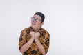 A spooked southeast asian muslim man loos around clenching his collar in fear. Wearing a batik shirt and songkok skull cap with