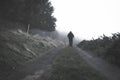 A spooky blurred ghostly hooded figure on a path in the countryside on a foggy day. With a muted, grainy edit Royalty Free Stock Photo