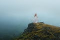 A spooky, blurred, ghostly woman with a white dress, standing on a cliff face looking out on a moody foggy day