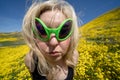 Spooky, creepy blonde woman wearing green alien sunglasses in a field of goldfield wildflowers in Carrizo Plain National Monument