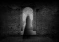 A spooky ghost of a woman in a dress, back to camera, framed by the archway of an old building. With a grunge, vintage, blurred