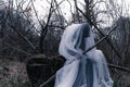 A spooky, ghostly hooded figure holding a wooden cross in a forest in winter