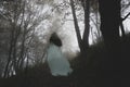 A spooky ghostly woman in a long white dress walking up a path through a moody misty autumn woodland Royalty Free Stock Photo