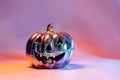 Spooky halloween pumpkin, Jack O Lantern, with an evil face and eyes made of holographic glass in neon lighting on pink