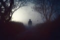 A spooky, horror concept. Of a scary shadow person with a hat standing in a country road. With trees silhouetted against the fog