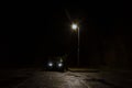 A spooky, mysterious hooded figure, standing next to a car under a street light at night