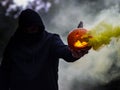 Spooky shot of a Caucasian guy holding a smoking Halloween pumpkin while wearing a facemask Royalty Free Stock Photo