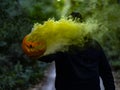 Spooky shot of a Caucasian guy holding a smoking Halloween pumpkin while wearing a facemask Royalty Free Stock Photo