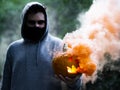 Spooky shot of a European guy holding a smoking Halloween pumpkin while wearing a facemask Royalty Free Stock Photo