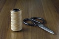 Spool of beige thread and scissors on a yellow wooden table surface