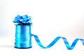 Spool of blue wavy ribbon and decorative gift bow on white background