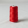A spool of bright red thread stands upright on a plain light-colored surface. The thread Royalty Free Stock Photo