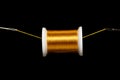 A spool of gold thread suspended on a field of black on a thread between 2 needle eyes. Plenty of space for copy