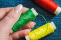 Spool of green sewing thread and a needle in a female hand against the background of other spools of thread on denim Royalty Free Stock Photo