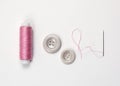 Spool of pink thread, needle, two buttons on a white background. Royalty Free Stock Photo