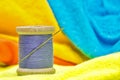 Spool of purple cotton thread and sewing needle sitting on bright colored clothing. Royalty Free Stock Photo