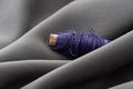 A spool with purple threads in a draped soft gray fabric, close-up, macro. Atelier, tailoring, sewing background. The Royalty Free Stock Photo