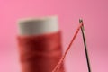 Spool with red thread and needle on pink background Royalty Free Stock Photo