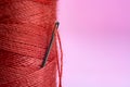 Spool with red thread and needle on pink background Royalty Free Stock Photo