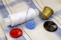 A spool of white thread with a needle, colored buttons and a thimble on the background of the shirt Royalty Free Stock Photo