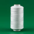 A spool of white thread stands vertically against a solid green background. The threa Royalty Free Stock Photo