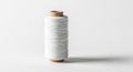 A spool of white thread stands vertically on a smooth, light-colored surface. The threa Royalty Free Stock Photo