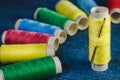 Spool of yellow thread with a needle on the background of spools of colored thread on a denim Royalty Free Stock Photo
