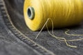 A spool of yellow thread and a needle on dark grey denim.