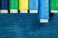 Spools of blue, yellow and green sewing thread arranged in row on denim with copy space