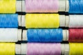 Spools of blue, yellow and pink sewing thread arranged in rows on denim