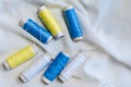 Spools of blue, yellow and white threads and sewing needle on white cotton cloth