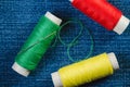 Spools of green, red and yellow threads and sewing needle on denim Royalty Free Stock Photo