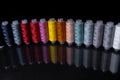 Spools with multi-colored threads stand in a row on a mirror surface. Royalty Free Stock Photo