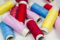 Spools of pink, yellow, blue and red threads and sewing needle on white cotton cloth