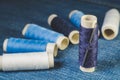 Spools of white and blue threads and sewing needle on denim