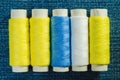 Spools of white, yellow and green sewing thread arranged in row on denim Royalty Free Stock Photo
