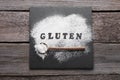 Spoon, board and word Gluten written with flour on wooden table, flat lay