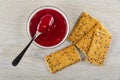 Spoon in bowl with cherry jam, crackers with flax seeds on wooden table. Top view