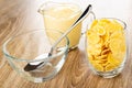 Spoon in bowl, pitcher with yogurt, glass with corn flakes on wooden table